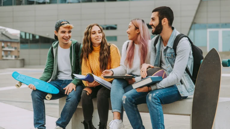 Studenti con libri e skateboard seduti fuori dalla scuola